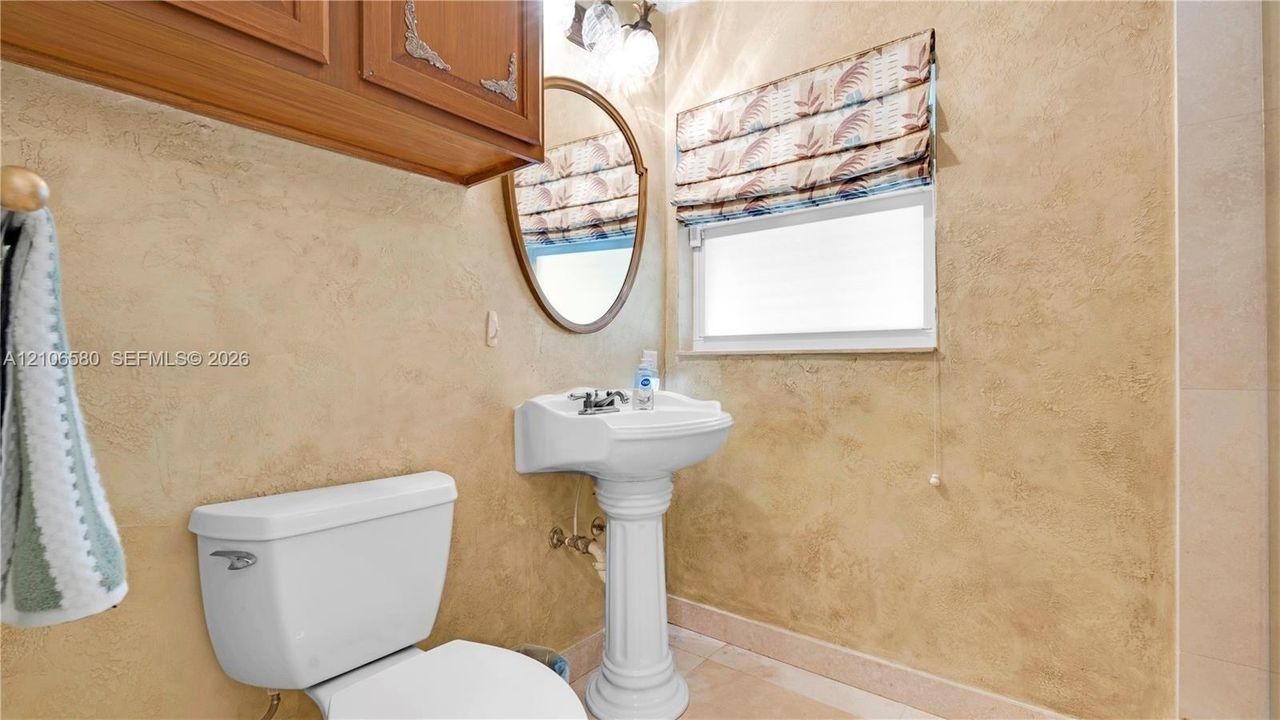Pedestal sink with chrome faucet, oval mirror, wall-mounted wood-finish cabinetry, and textured wall treatment