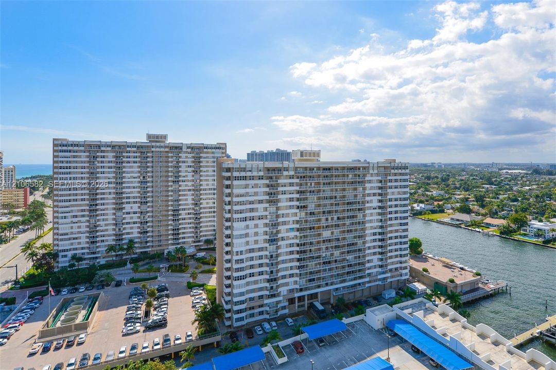 High-rise residential buildings situated on a waterfront parcel featuring surface parking, covered parking structures, and bulkhead hardscaping