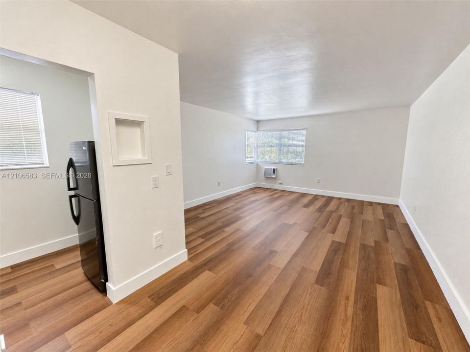 Open-concept interior featuring wood-finish flooring, crisp white walls, dual windows, and built-in wall niche cabinetry