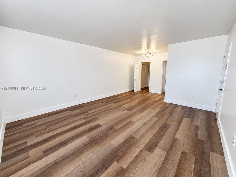 Neutral-toned interior space featuring wood-finish flooring, crisp white walls, a multi-arm flush-mount light fixture, and interior doors