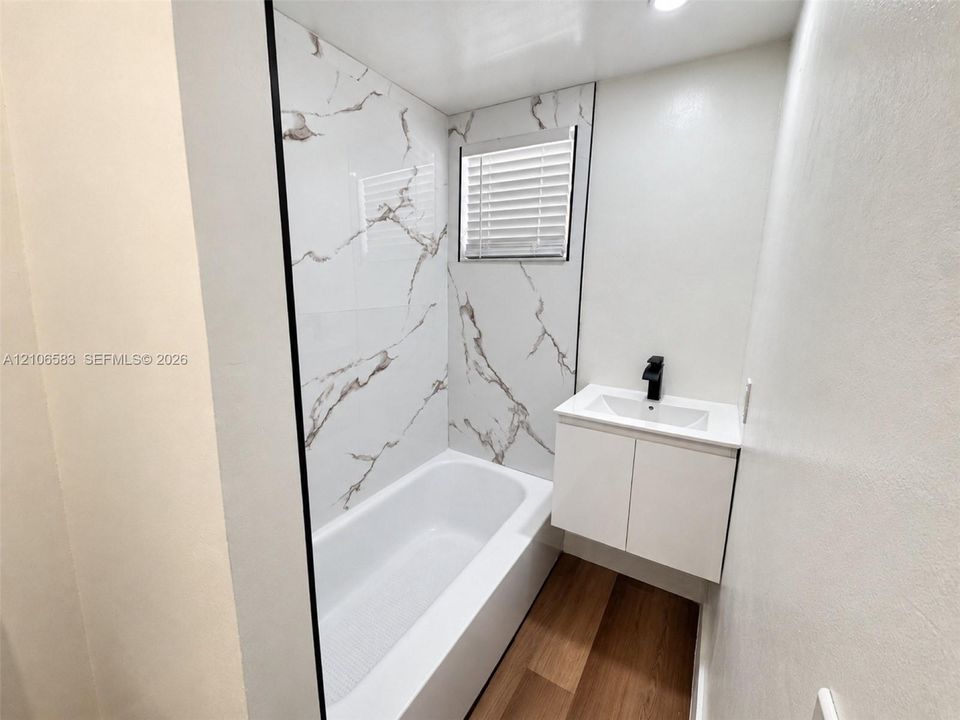 Bathroom featuring floor-to-ceiling porcelain tile tub surround, wall-mounted floating vanity with integrated sink, matte black faucet, and wood-finish flooring