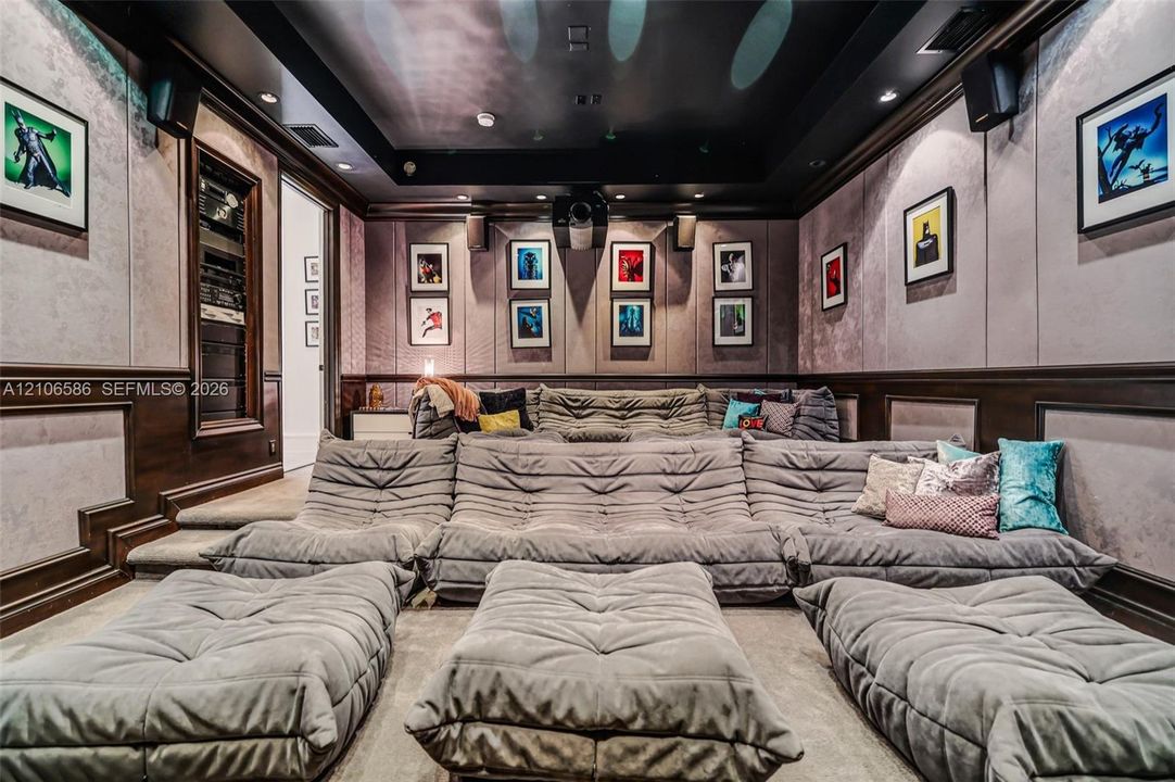 Media room featuring tiered flooring, fabric-paneled walls, built-in A/V rack, recessed ceiling lighting, and crown molding