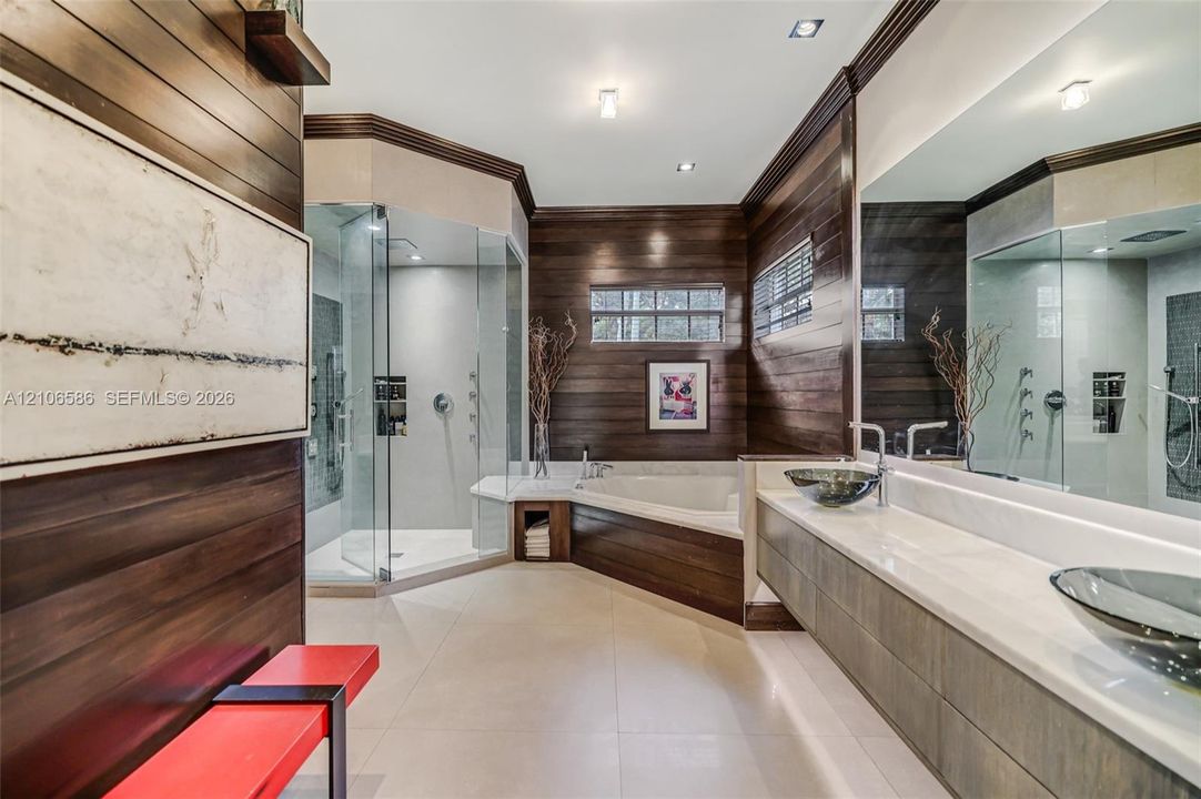Custom bathroom featuring wood-paneled walls, a glass-enclosed shower, a jetted soaking tub, floating vanity with dual glass vessel sinks, and light-toned tile flooring