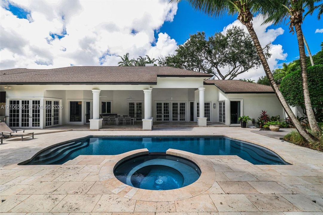 Covered patio with architectural columns, stone paver decking, and in-ground swimming pool featuring an integrated circular spa