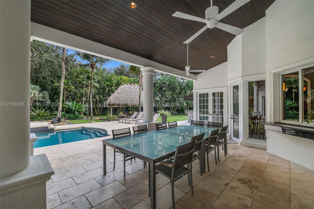 Covered patio featuring stone-tile flooring, a wood-paneled ceiling, ceiling fans, and structural columns