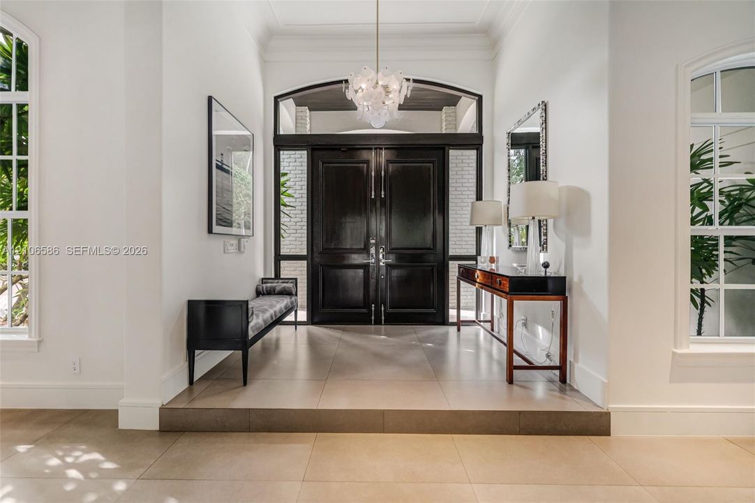 Foyer featuring large-format tile flooring, a set of double entry doors with transom window, oversized arched windows, and an ornate glass chandelier