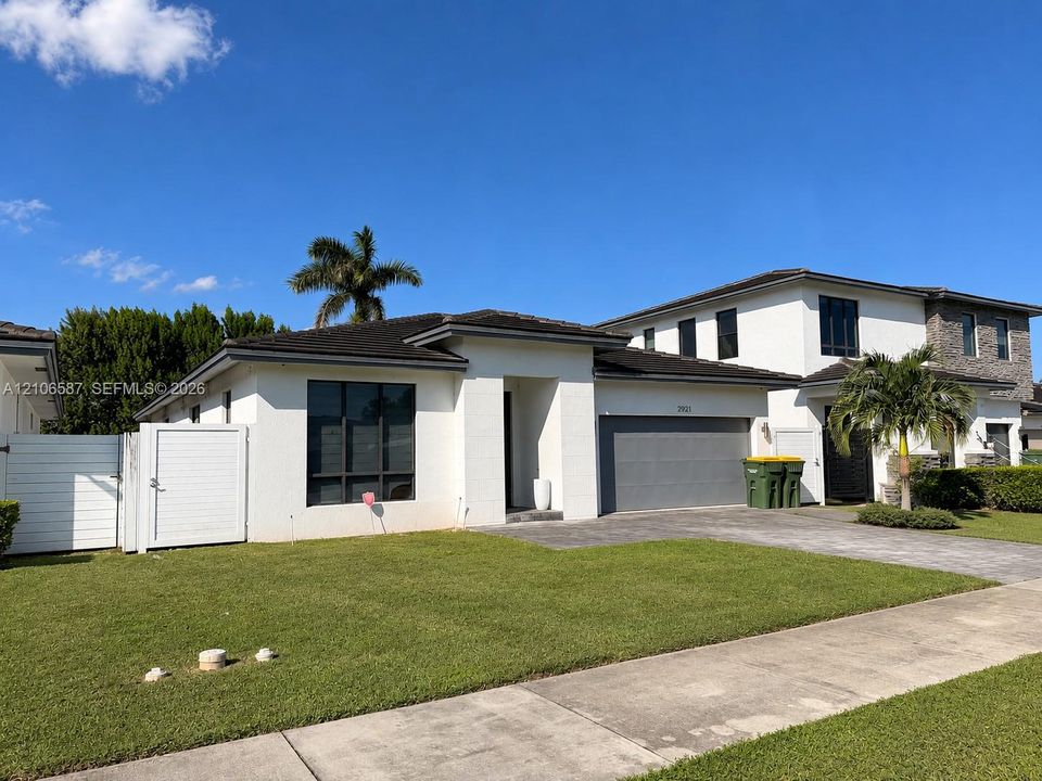 Single-story exterior featuring white stucco siding, a multi-car garage, a paver driveway, and a white privacy fence