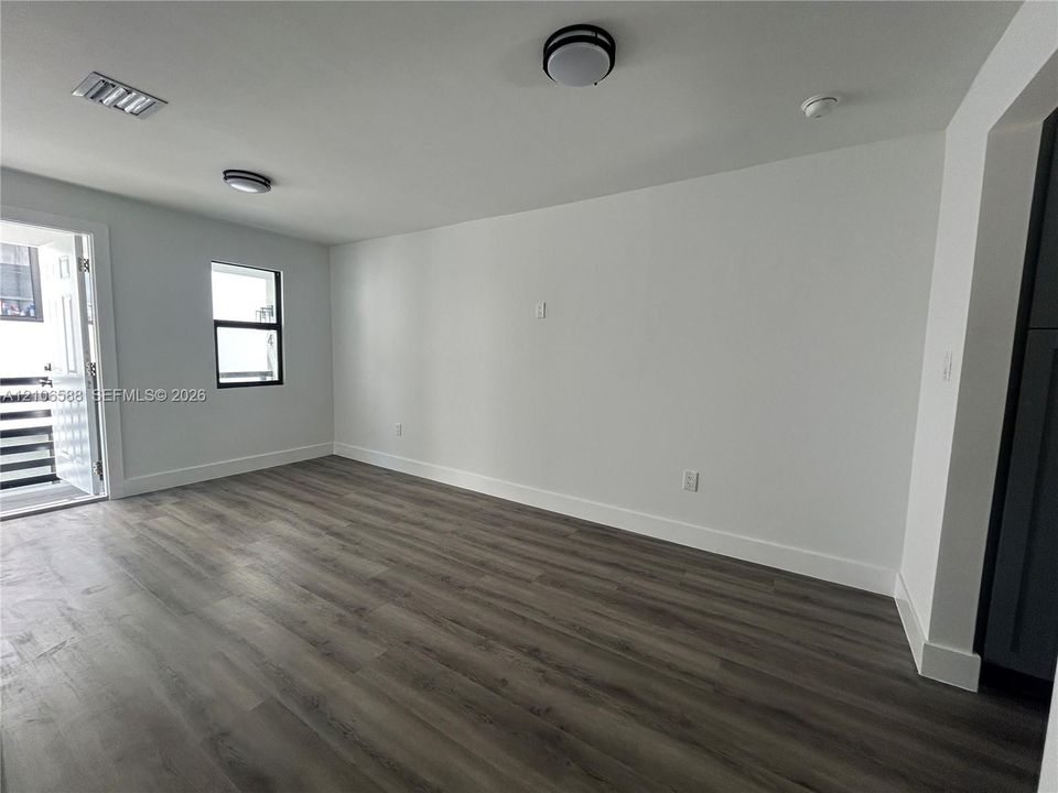 Interior space featuring wood-finish flooring, white walls, dual flush-mount ceiling light fixtures, and a single-pane window