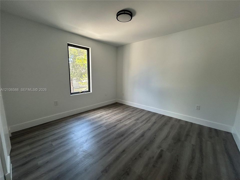 Room featuring wood-finish flooring, a single window with a dark frame, and a flush-mount overhead light fixture