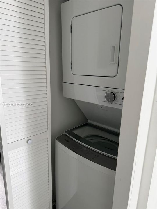 Stacked laundry unit housed within a closet featuring white louvered doors