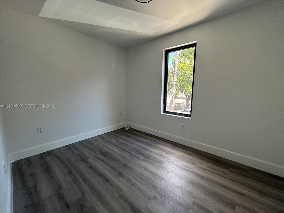 Neutral interior space featuring wood-finish flooring, smooth-finish walls, and a tall rectangular window with a black frame