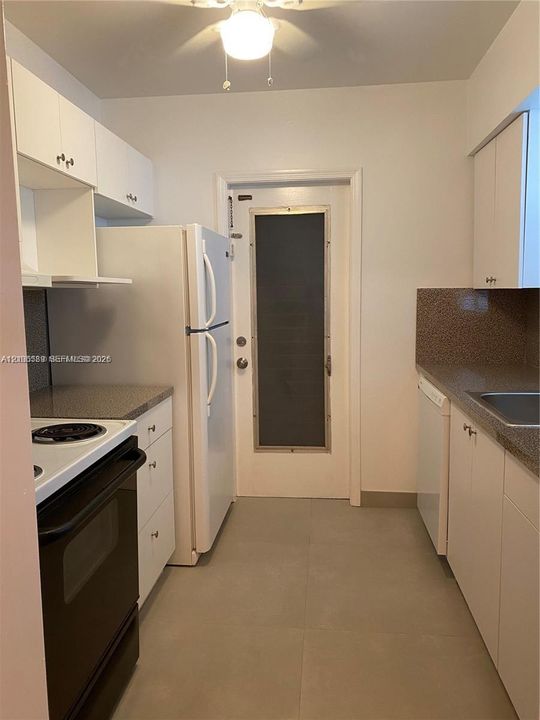 Kitchen featuring white cabinetry, speckled stone-finish countertops, stainless steel sink, large-format neutral tile flooring, and a glass-paneled exterior door