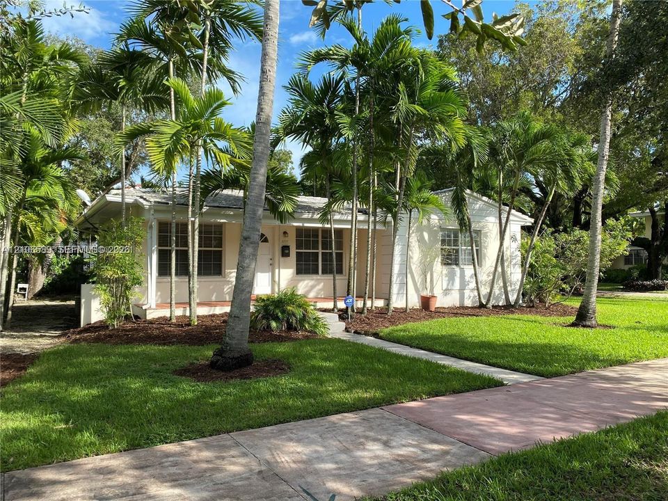 Single-story residence featuring a light-toned exterior, concrete walkway, and expansive lawn with mature palm trees