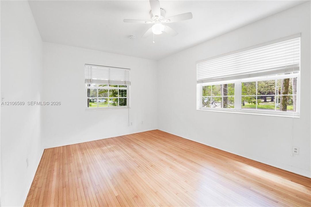 Interior room featuring wood-finish flooring, white walls, a ceiling-mounted light fixture with fan, and windows equipped with horizontal blinds