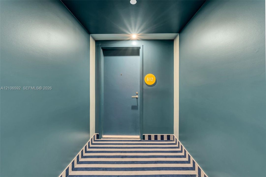 Entryway featuring saturated wall paint, a recessed ceiling light, a solid door with metallic hardware, and a striped carpet runner