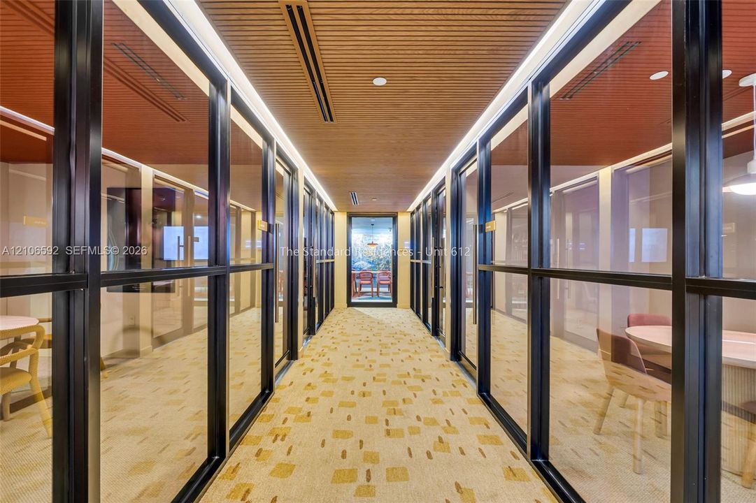 Hallway featuring floor-to-ceiling glass partitions with black frames, linear wood-slat ceiling, recessed lighting, and patterned wall-to-wall carpeting