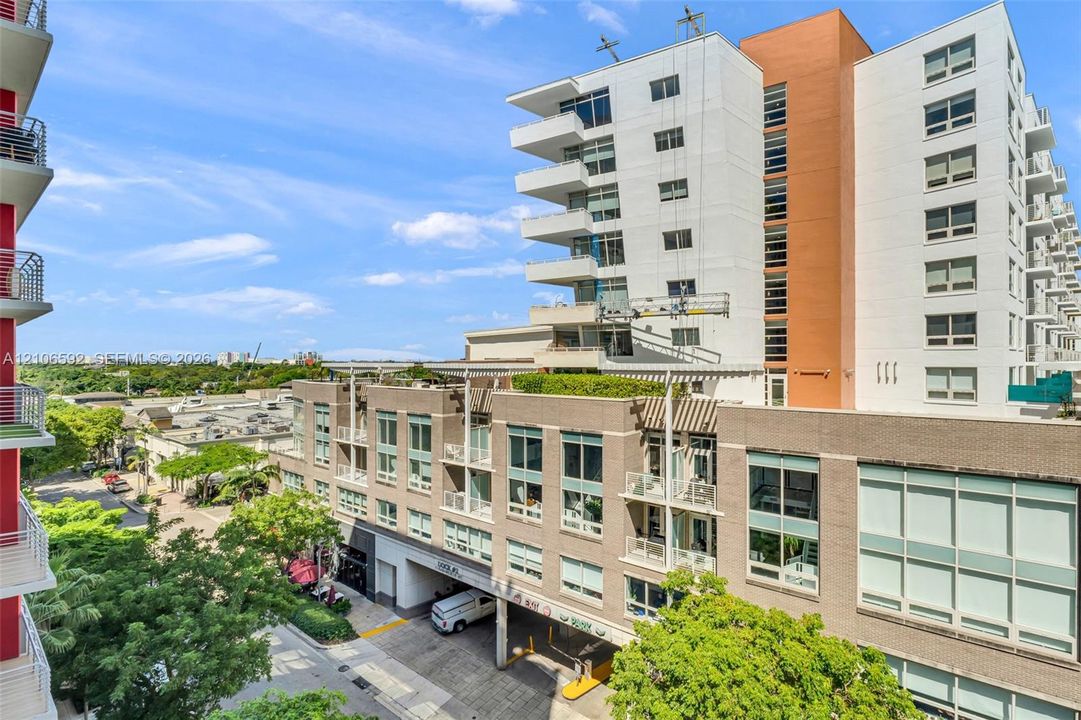 Mid-rise building exterior featuring a textured masonry facade, extensive floor-to-ceiling windows, private balconies, and an integrated structural trellis