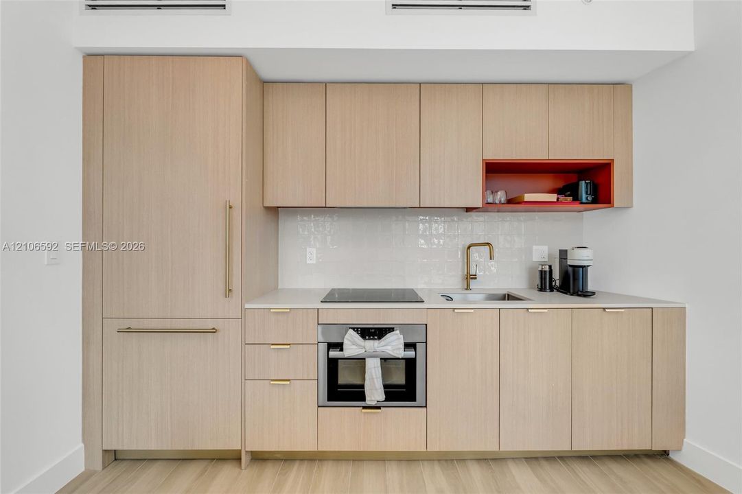 Kitchen featuring light wood-finish cabinetry, a white tile backsplash, a stone-finish countertop, integrated refrigerator, and a recessed display niche