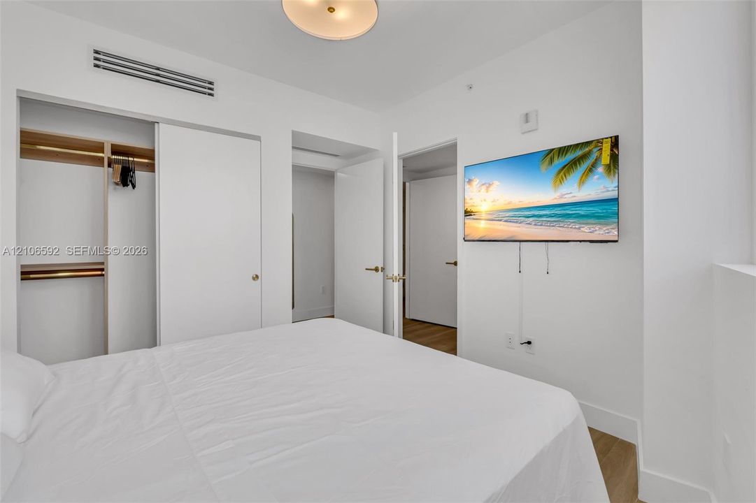Room featuring wood-finish flooring, ceiling-mounted light fixture, sliding door closet with built-in shelving, and integrated climate control unit