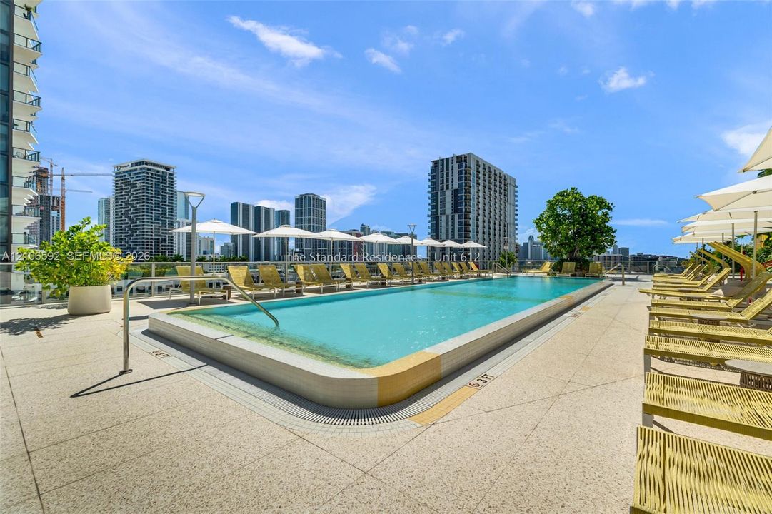 Rooftop swimming pool featuring a tiled perimeter, integrated drainage, glass panel railings, and expansive paved deck surfacing