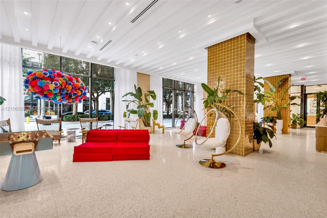 Expansive open-concept lobby featuring floor-to-ceiling windows, polished light-toned flooring, ribbed ceiling detailing with recessed lighting, and structural columns finished in gold-toned square tile