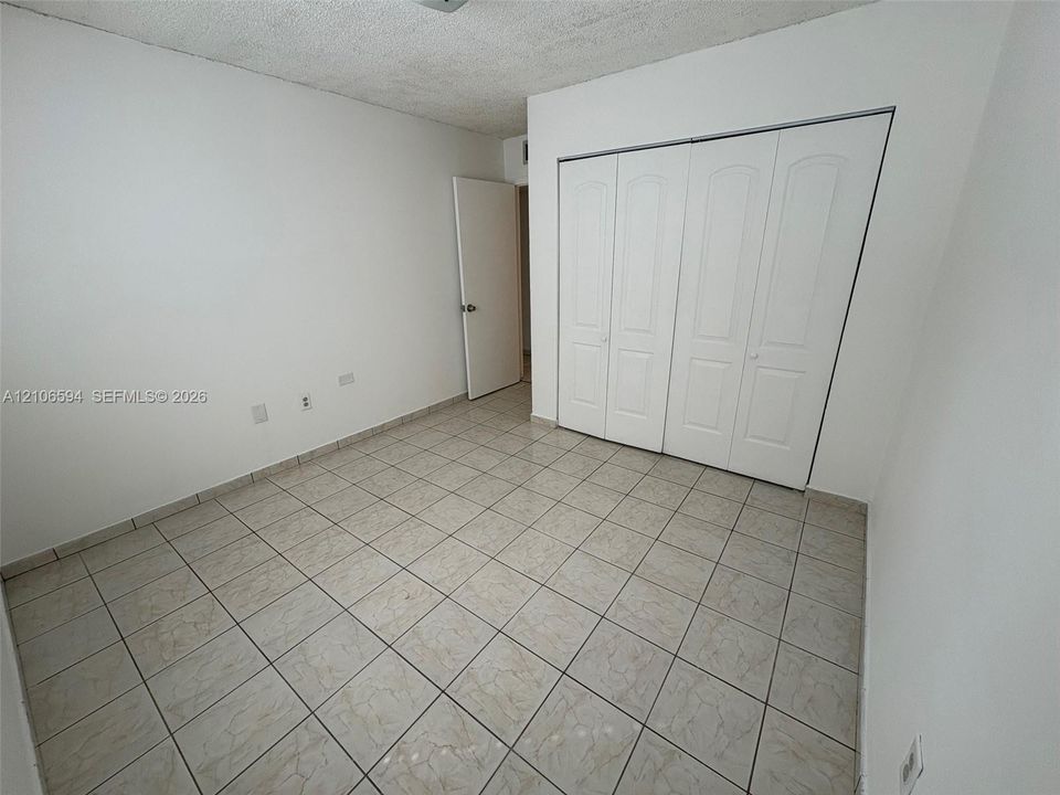 Room featuring neutral wall-to-wall ceramic tile flooring, four-panel bi-fold closet doors, and textured ceiling finish