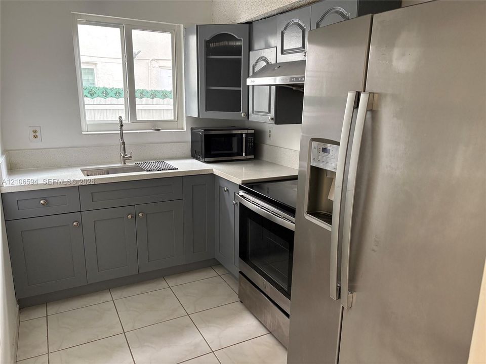 Kitchen featuring gray shaker-style cabinetry, white solid-surface countertops, stainless steel appliances, and tile flooring