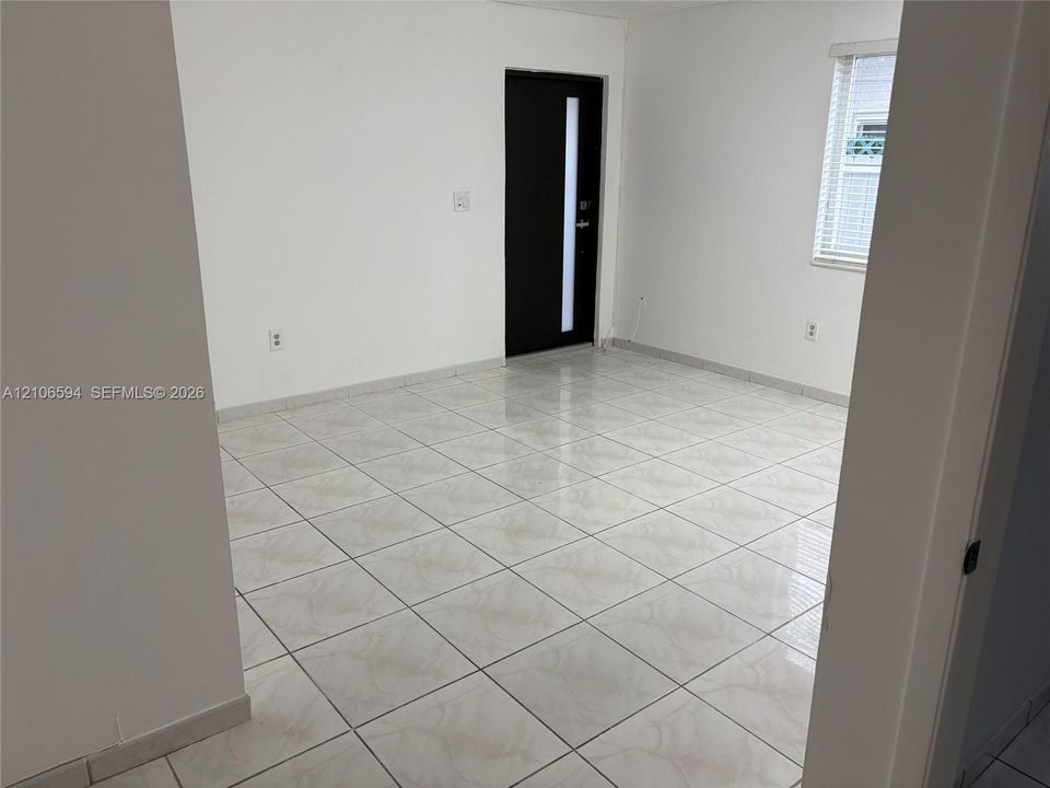 Polished tile flooring, neutral wall finishes, and a dark-toned entry door featuring a vertical glass inlay, complemented by a horizontal window with adjustable blinds