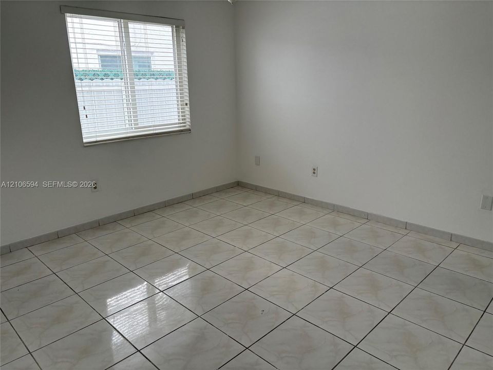 Neutral interior room featuring large-format ceramic floor tiles, white wall finishes, and a single-pane window with integrated horizontal blinds