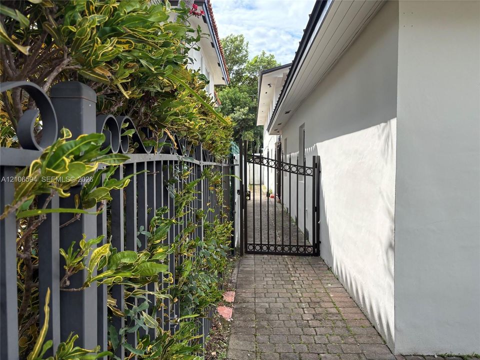 Side exterior passage featuring stone paver walkways, decorative metal fencing, and an integrated metal security gate