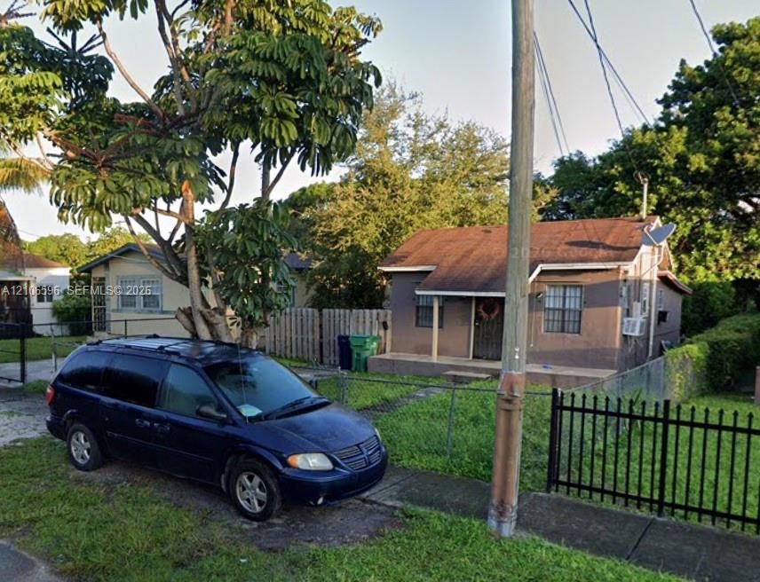 Single-story exterior featuring a shingled gable roof, covered front porch, and perimeter metal fencing