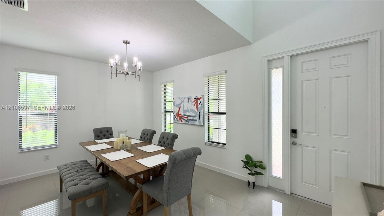 High-ceiling entryway featuring neutral tile flooring, multi-paneled door with integrated glass sidelight, and a decorative multi-arm chandelier