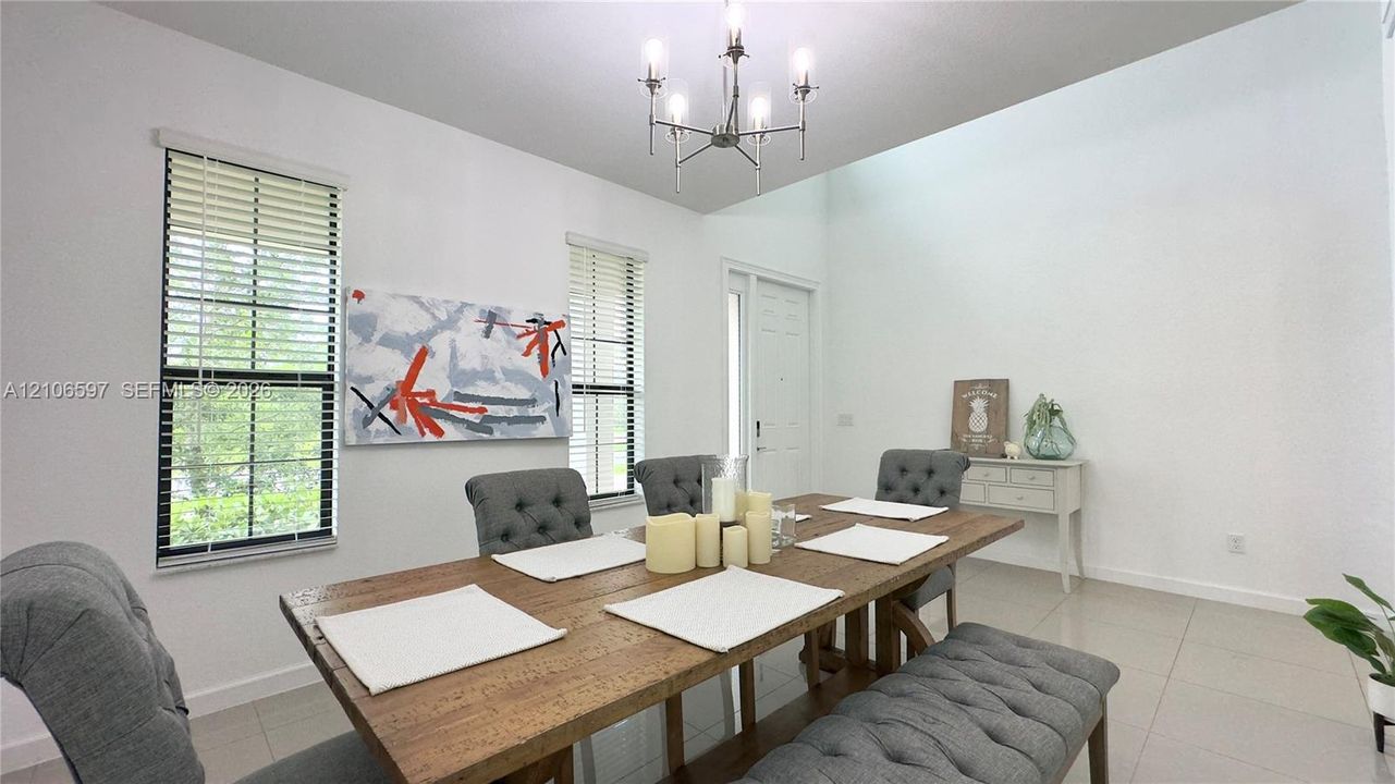 High-ceiling room featuring large windows, neutral tile flooring, and a multi-arm chandelier