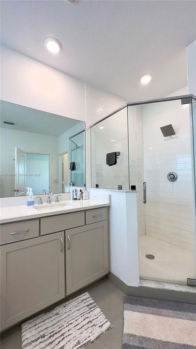 Bathroom featuring a vanity with light-tone cabinetry and white countertop, recessed lighting, wall-to-wall mirror, and a glass-enclosed shower with white wall tile and a square shower head