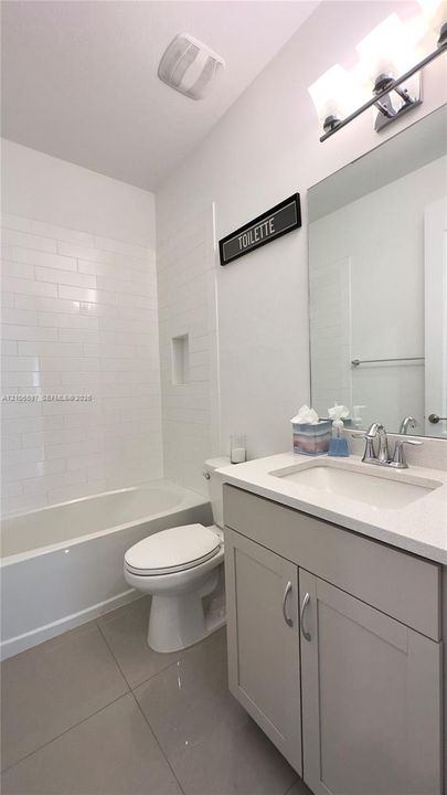 First floor guest  Bathroom featuring a white subway tile shower surround with an integrated recessed niche, light gray cabinetry, a neutral stone-finish countertop, and polished chrome fixtures