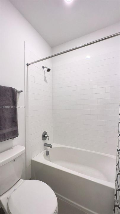 Upstairs guest bathroom Full-size bathtub featuring white subway-style wall tiling, a wall-mounted shower head, and a chrome-finish diverter faucet