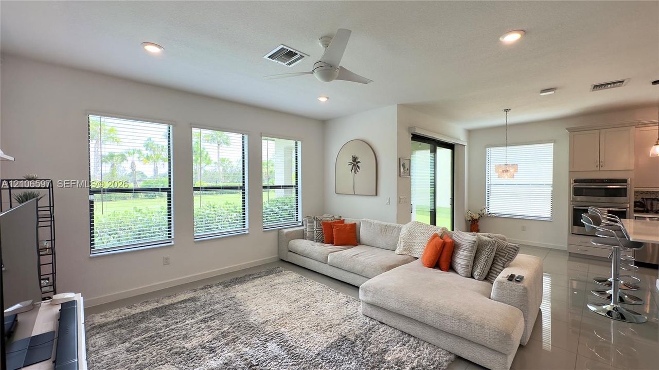 Open concept living area featuring polished tile flooring, multiple windows with horizontal blinds, recessed lighting, and a kitchen equipped with built-in wall ovens and an island
