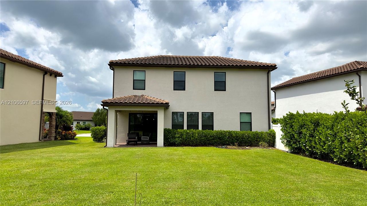 Two-story exterior featuring a tile roof, stucco finish, covered patio, and manicured lawn with privacy hedging