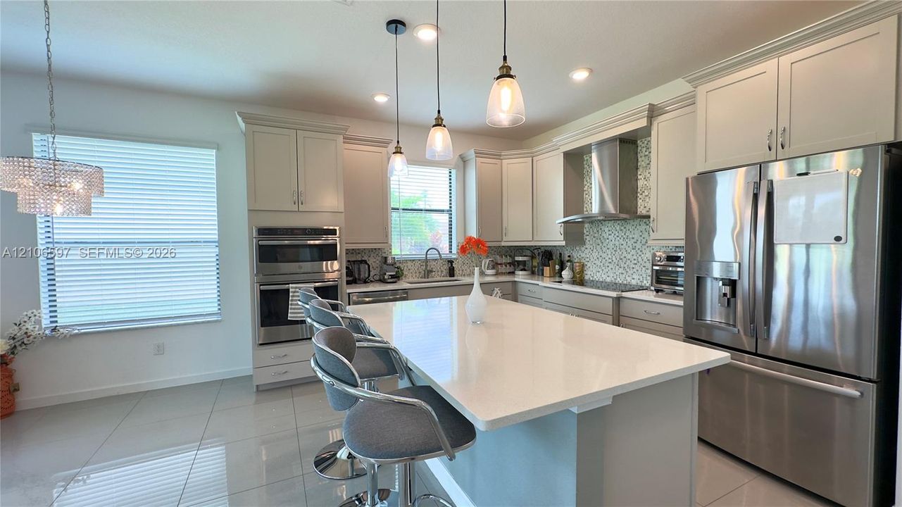 Kitchen featuring a central island with quartz countertops, custom shaker-style cabinetry, stainless steel built-in double ovens, a glass-tile backsplash, and recessed and pendant lighting