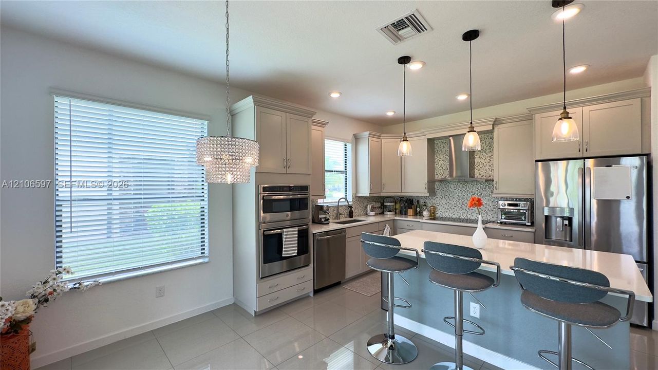 Kitchen featuring light-toned cabinetry, stainless steel appliances, quartz countertops, a stone-tile backsplash, and suspended pendant lighting