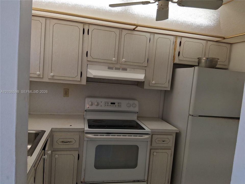 Kitchen featuring white cabinetry, solid-surface countertops, integrated range hood, electric range, and ceiling-mounted fan
