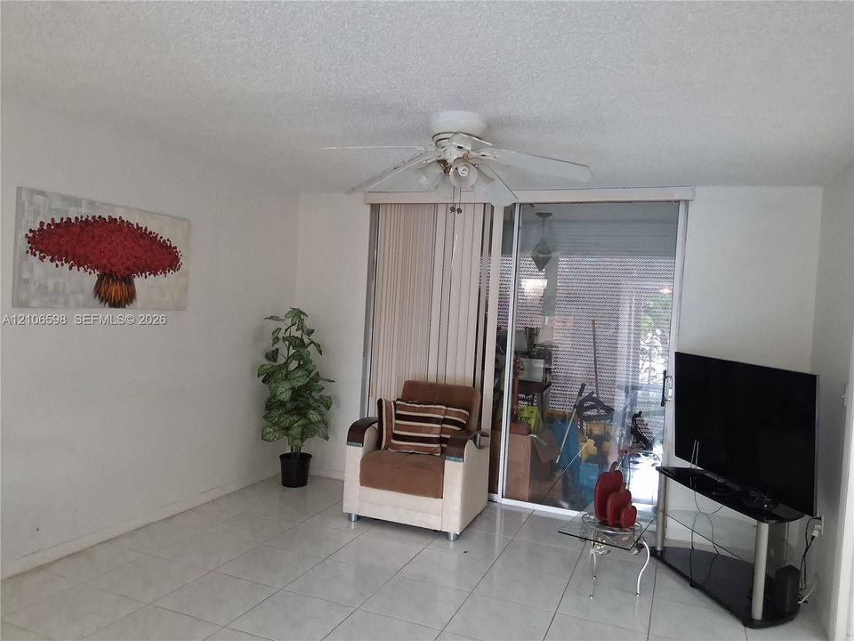 Interior space featuring neutral tile flooring, a ceiling fan with integrated lighting, and a floor-to-ceiling glass sliding door