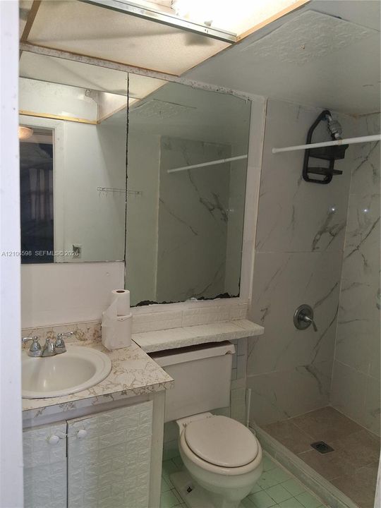 Bathroom featuring a vanity with a drop-in sink, stone-finish countertop, large wall-mounted mirror, and a shower enclosure with large-format tile surround