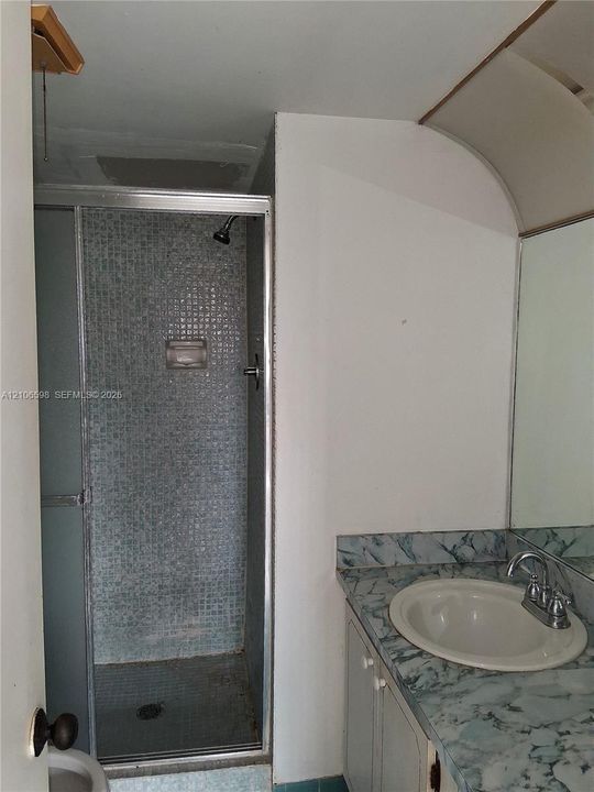 Bathroom featuring a glass-enclosed shower with mosaic tile surround, vanity with an integrated basin, and a wall-mounted mirror