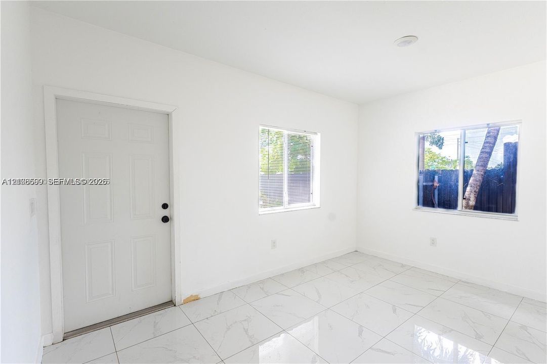 Interior space featuring large-format white stone-finish tile flooring, two windows with natural light, and a white paneled entry door