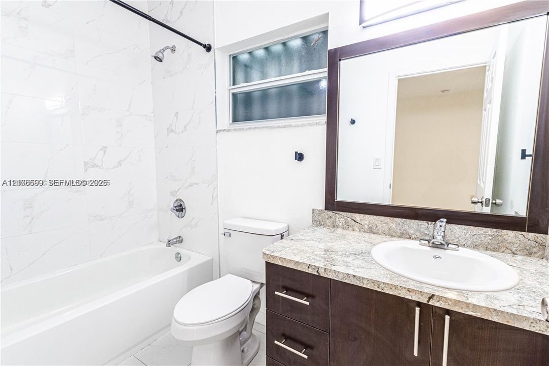 Bathroom featuring stone-finish countertop, dark wood-finish cabinetry, rectangular mirror with dark frame, and full-height wall tile surrounding the bathtub