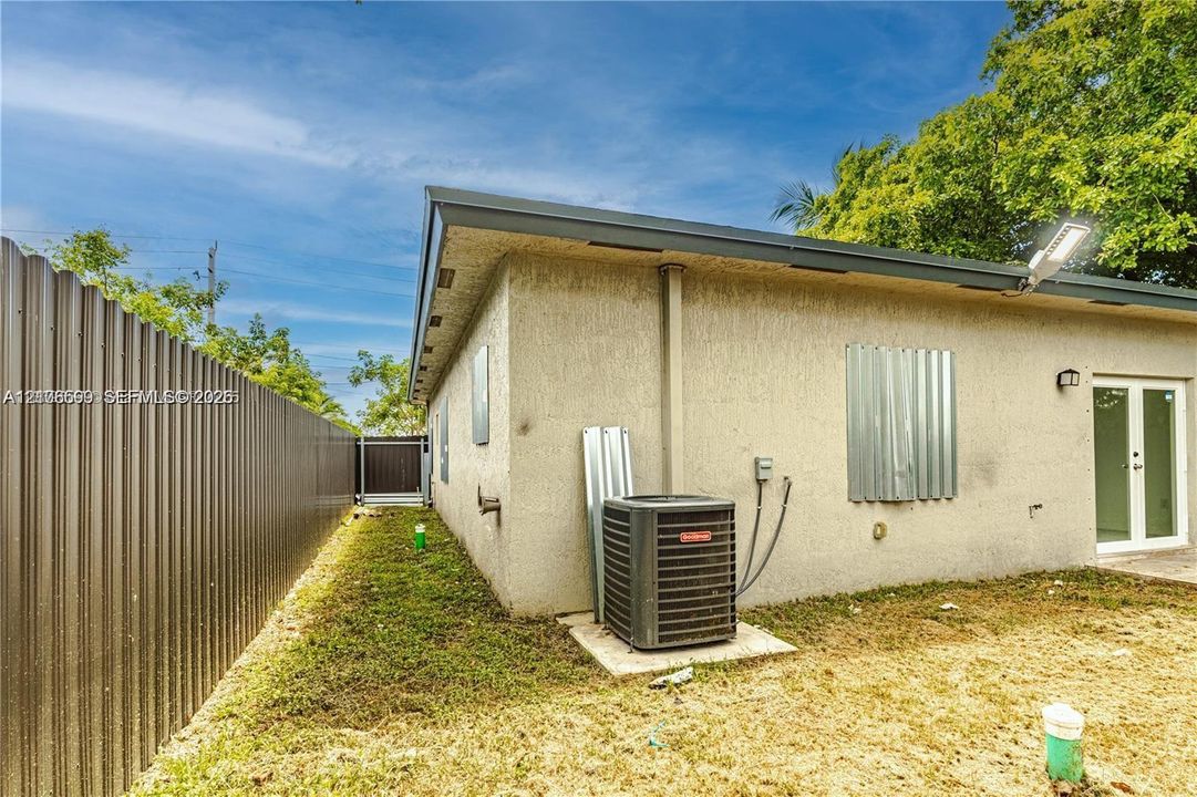 Stucco exterior featuring corrugated metal perimeter fencing, double glass-panel entry door, and exterior wall-mounted lighting