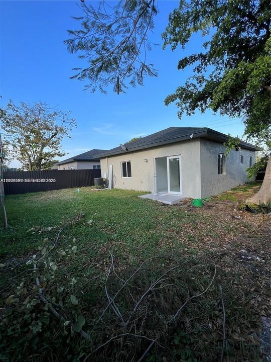 Exterior structure with a stucco finish, hip roof, sliding glass door, and a perimeter privacy fence