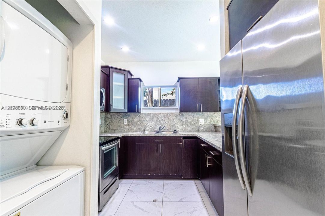 Kitchen featuring dark wood-finish cabinetry, stone-patterned countertops, stainless steel appliances, tile flooring, and integrated laundry closet
