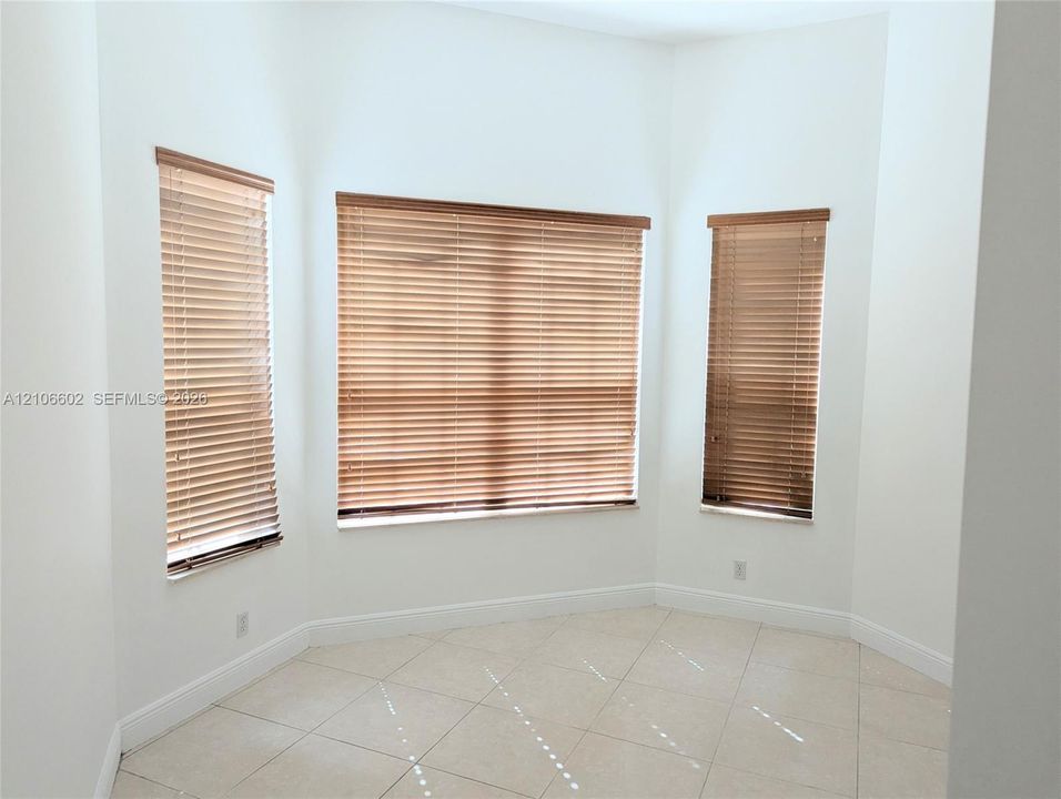 Bay window with three rectangular windows, neutral-tone tile flooring, and installed horizontal blinds